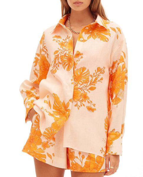 A person wearing a Kate Ford Hester Oversized Shirt with orange floral patterns and matching shorts, featuring dropped shoulders, stands against a white background.