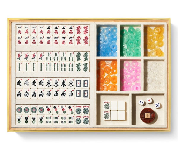 The AERIN Luxe Shagreen Mahjong Set in Cream is elegantly arranged in a luxurious shagreen box, featuring engraved tiles, small dice, and colorful chips placed in dedicated compartments.