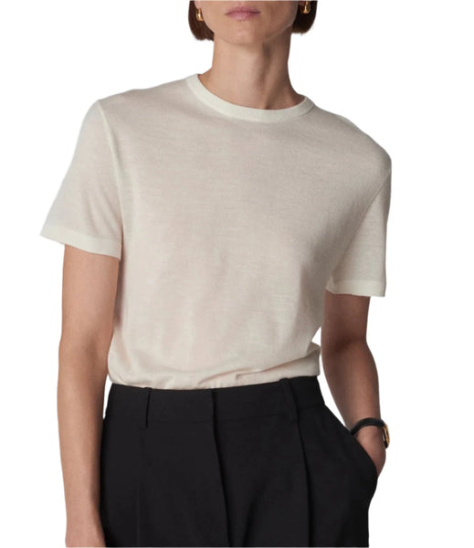 A person wearing a CO Cashmere Tee in plain white, part of the CO collection, is tucked into black trousers. A black wristwatch is visible on their left wrist, and the background is plain white.