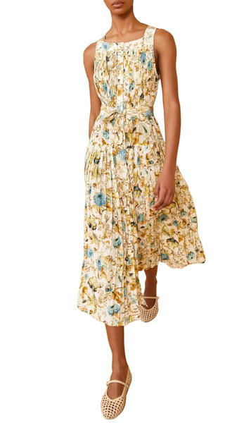 A person wearing the Ulla Johnson Annabeth Dress, a sleeveless, floral-printed midi dress with 19th century French florals on a pleated skirt, paired elegantly with beige woven shoes.