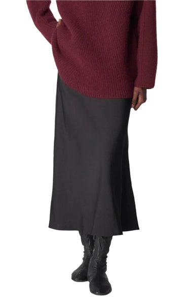 Person wearing a maroon sweater, long black boots, and the CO Slip Skirt by CO, designed for day-to-night versatility, standing against a plain white background.