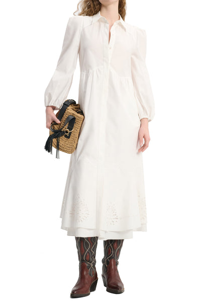 Person wearing a long white Dorothee Schumacher Poplin Power Dress with puffed sleeves, patterned knee-high boots, and holding a straw handbag with black fringe detailing.