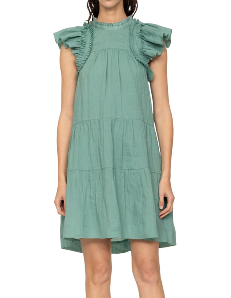 Woman wearing a sleeveless, teal-colored Sea NY Risa Tunic Dress with ruffled sleeves and a tiered mini skirt.