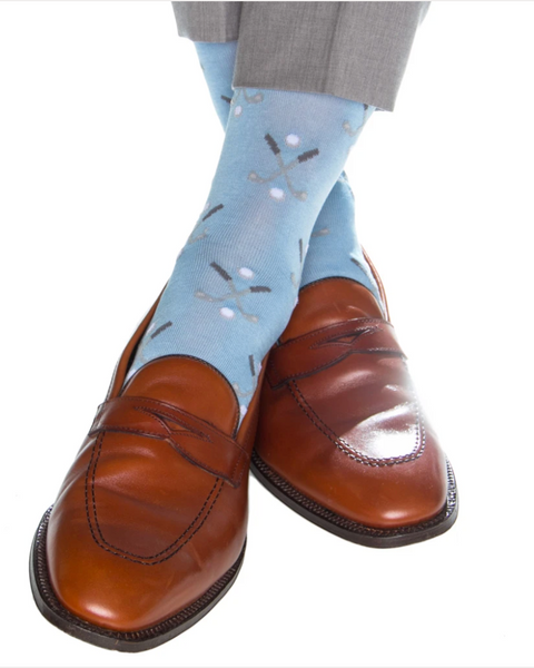 Wearing grey dress pants and brown leather dress shoes, this individual sports blue socks featuring crossed golf club designs. These Dapper Classics Golf Club Mid Calf Socks, Sky Blue by Dapper Classics offer a mid-calf fit and are made from breathable material, ensuring comfort throughout the day.