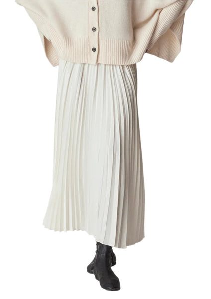 Person wearing a beige buttoned cardigan paired with the CO Pleated Elastic Waist Skirt by CO, a long white skirt made of Japanese stretch crepe, accompanied by black ankle boots. The image is cropped to show from the shoulders down.