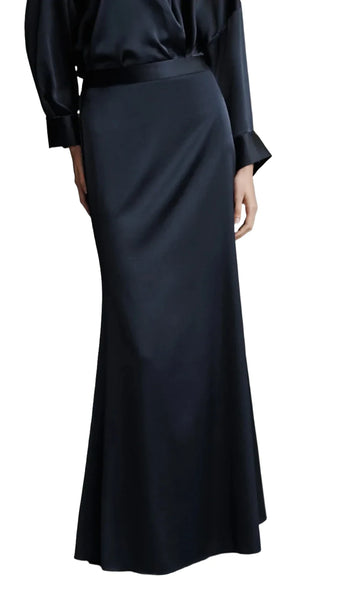 A person is shown from the neck down, wearing a sleek silk charmeuse black blouse paired with a floor-length black **TWP At Last Silk Skirt** by **TWP**.