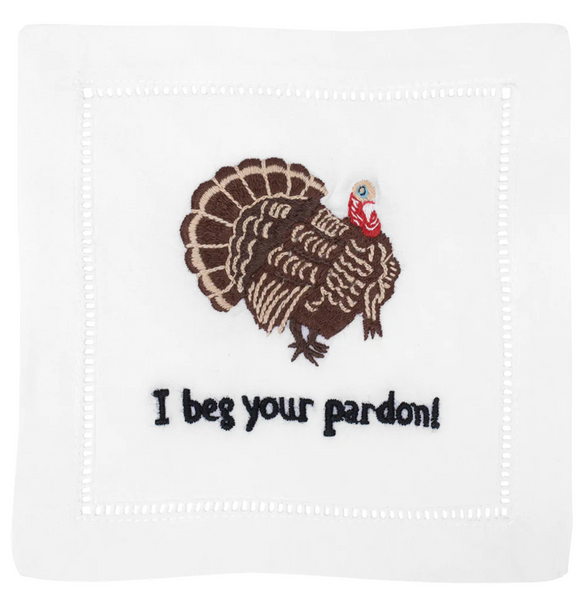 Embroidered turkey with a red and white hat on a white cloth, above the text "I beg your pardon!" in black letters - a perfect custom August Morgan Cocktail Napkins I Beg your Pardon!, Set of 4 hostess gift for Thanksgiving.