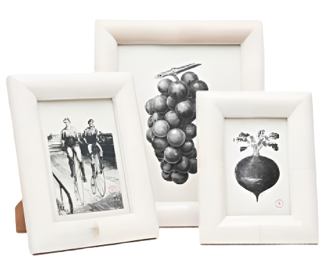 Three framed Pigeon & Poodle Vannes Frame Collection black-and-white artworks; two depict fruit clusters and one shows two men cycling, all set in beveled bone frames.