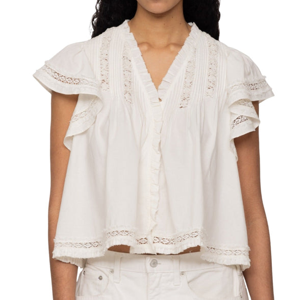 A person is wearing a Sea NY Lilith Top with ruffled sleeves, a V-neckline, and lace details. The cotton blouse is paired with white pants.