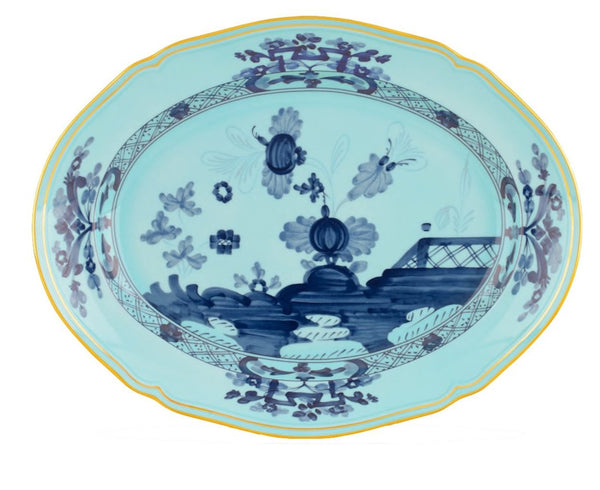 The GINORI 1735 Oriente Italiano Iris Oval Platter by Ginori 1735 showcases detailed dark blue floral and nature-themed designs, enhanced by a geometric border pattern. The rim of this elegant platter is highlighted with a striking yellow outline.