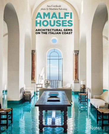 Cover of the book "Amalfi Houses: Architectural Gems on the Italian Coast" by Ana Cardinale, published by Rizzoli. It features an airy, white-walled room with turquoise ceramic floors, columns, and a central wooden table, capturing the essence of cliff-side villages along the Amalfi Coast.