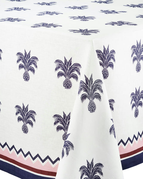 Introducing the Aquazzura Ananas Blue Tablecloth by Aquazzura Casa: a white, 100% linen tablecloth adorned with a repeating pattern of blue pineapple motifs and a border featuring zigzag and stripe designs in rich blue and red tones. Elevate your dining experience with this piece of luxury tableware.