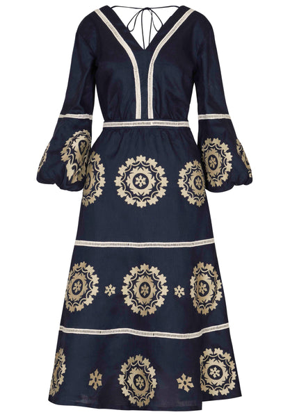 A long-sleeved Andres Otalora Mapa Midi Dress in dark blue, with a V-neckline featuring beige embroidered detailing and circular floral patterns, complete with a tie at the neck.