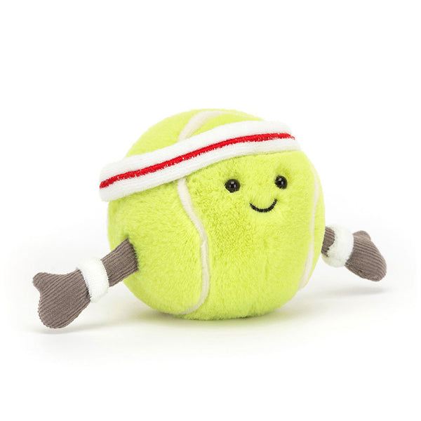 A Jellycat Amuseable Sports Tennis Ball by Jellycat resembling a tennis ball with a happy face, perfect for any tennis enthusiast, wearing a white headband with a red stripe and white wristbands, and having gray fabric arms.