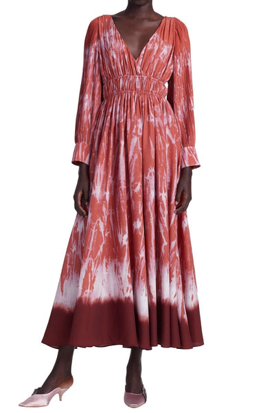 Person wearing an Altuzarra Kathleen Dress by Altuzarra with a V-neckline and a ruched waist. The dress has a reddish-brown and white tie-dye pattern. They are also wearing pink heeled shoes.