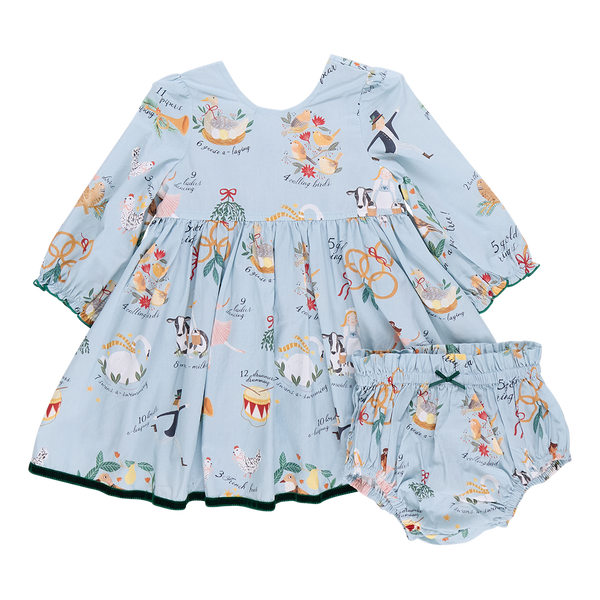 The Pink Chicken Baby Girl Amma Dress showcases a light blue children's dress embellished with festive illustrations such as animals and musical instruments, reminiscent of the "12 Days of Christmas." It includes matching bloomers, making it ideal for your little one's holiday celebrations.