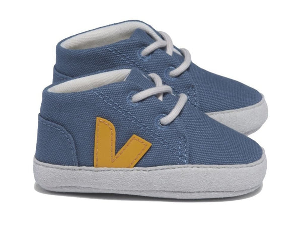 The Veja Baby Canvas Sneakers by Veja are a pair of blue baby sneakers with white soles and laces, featuring a yellow 'V' logo on the side, crafted from vegan suede and organic cotton.