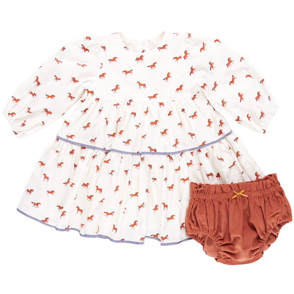 A baby girl's white long-sleeve Pink Chicken Julia Dress featuring a charming red horse pattern, paired with rust-colored bloomers adorned with chambray detailing.