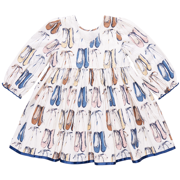 Charming and elegant, the Pink Chicken Girls' Amma Dress by Pink Chicken features a long-sleeved design with a colorful all-over print of ballet shoes in shades of blue, pink, and brown on a white background, complemented by a delicate blue ribbon detail.