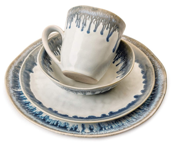 A Simon Pearce Burlington Pool Collection from Simon Pearce featuring a rustic mug, bowl, salad plate, and dinner plate, all adorned with blue and gray organic drip glaze patterns.