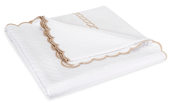 Folded quilt from the Matouk Classic Chain Scallop Matelassé Bedding Collection in Dune, featuring scalloped edges, Petra diamond matelassé, and a decorative embroidered border by Matouk.