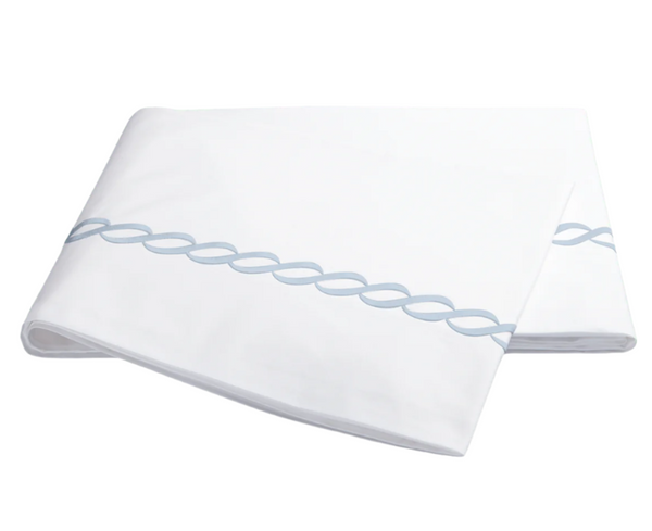 The Matouk Classic Chain Bedding Collection in light blue includes a folded white 350 thread count cotton percale sheet, featuring an interlocking rope pattern on the edge. It's OEKO-TEX certified for comfort and quality.