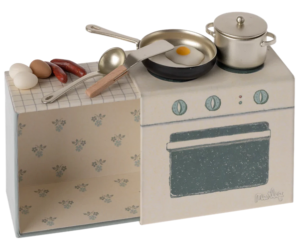 A Maileg Cooking Set designed for mice, featuring a miniature toy stove with a frying pan containing a sunny-side-up egg, a pot, sausages, and three eggs on the countertop. This small kitchen set includes kitchen utensils and an oven, all set against a floral-patterned background—perfect for any kids playset.