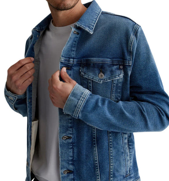 A person wearing the AG Dart Jacket by AG Jeans over a white shirt is adjusting the buttons with both hands. The classic comfort stretch denim and adjustable waist tabs add to its appeal and fit.