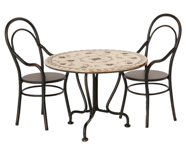 The Maileg Dining Table Set by Maileg includes a round dining table with a decorative pattern, accompanied by two sturdy matching metal chairs that feature curved backrests and legs.