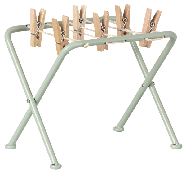 The Maileg Drying Rack with Pegs, Miniature by Maileg is a small, light green foldable rack perfect for handling your laundry routine. Ideal for drying everything from delicate teddies and bunnies to everyday garments, this practical and charming rack features multiple wooden clothespins attached to it.