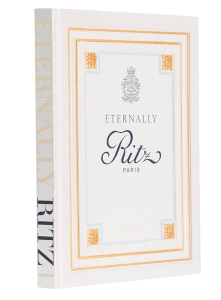 The image shows a book titled "Eternally Ritz Paris" with a white cover featuring ornate gold and blue detailing and the Ritz logo. The spine reads "Eternally Ritz" in large, light grey font, evoking the timeless elegance of the luxury hotel located at Place Vendôme. The book is published by Assouline.