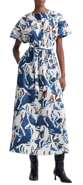 A person wearing an Altuzarra Altuzarra Paulina Dress, a long blue, white, and brown equestrian print dress with kimono-style sleeves, cinched at the waist with a matching belt, and black boots.