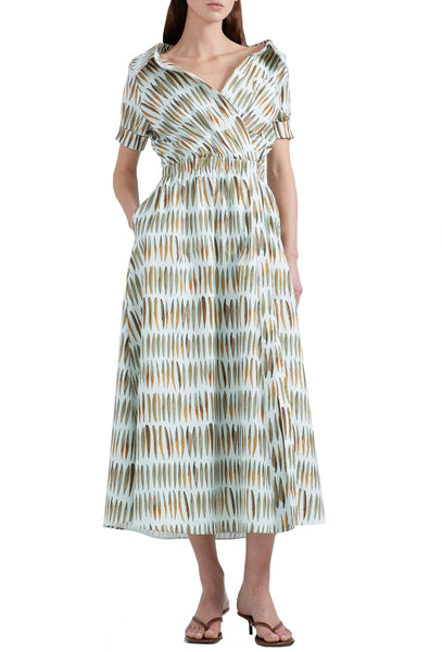 A person is wearing a long, patterned Altuzarra Lydia Dress with short sleeves and is standing with their back to the camera. The midi silhouette features a cinched waist and a spread collar, made from airy cotton poplin that adds an elegant touch to the ensemble.