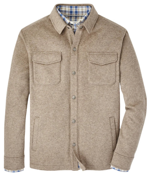 The Peter Millar Crown Flex Fleece Shirt Jacket, a men's beige wool jacket by Peter Millar, is crafted from Merino wool and features two chest pockets. It stands against a white background with an open collar that reveals a blue and white plaid lining, adding a stylish contrast.