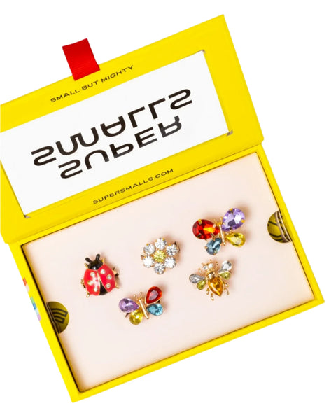 The Super Smalls Garden Get Together Ring Set by Super Smalls comes in a yellow box and includes five colorful, insect-themed jewelry items, featuring ladybug and butterfly rings as well as bee rings, all adorned with vibrant gemstone decorations.