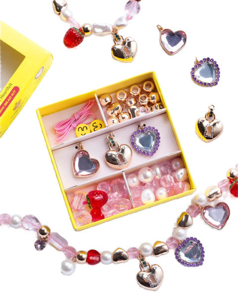 The Super Smalls Make It Heartfelt Mini Bead Kit by Super Smalls comes in a yellow box and includes an assortment of heart-shaped charms, beads, and threads for DIY jewelry making. It also features two partially finished beaded bracelets with special heart-shaped pendants displayed nearby.