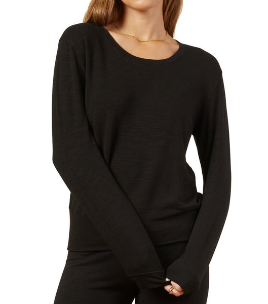 A person wearing a long-sleeved Monrow Supersoft Crew Neck Sweatshirt in black and matching black pants, with their left hand partially tucked into the supersoft fabric sleeve.