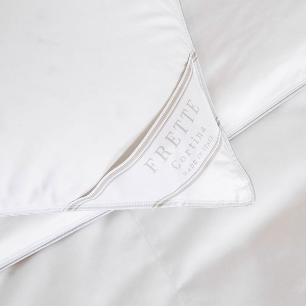 Close-up of a white Frette Cortina Pillow Insert, Medium Density made of sumptuous cotton sateen, featuring a label reading "Frette Cortina Made in Italy." The corner of the pillow insert is folded over to display the label.