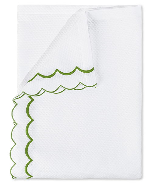 A neatly folded white towel with green double-scalloped edges and a textured diamond pique pattern from the Matouk India Pique Bedding Collection, Grass.