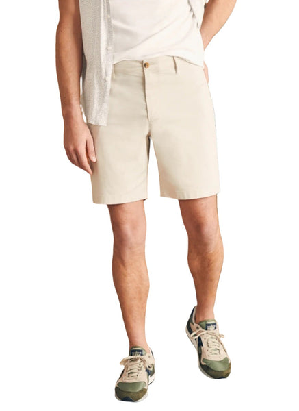 A person wearing a white shirt, Faherty Movement Chino Short 8" by Faherty with an elasticated interior waistband, and green sneakers. Only the lower half of their body is visible.