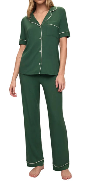 Dressed in the Eberjey Gisele Short Sleeve Long Pant PJ Set, an individual showcases a traditional men's pajama style featuring short sleeves and white piping. This ensemble, crafted from temperature-regulating knit fabric, emphasizes comfort and sustainability with its use of TENCEL™ Modal.