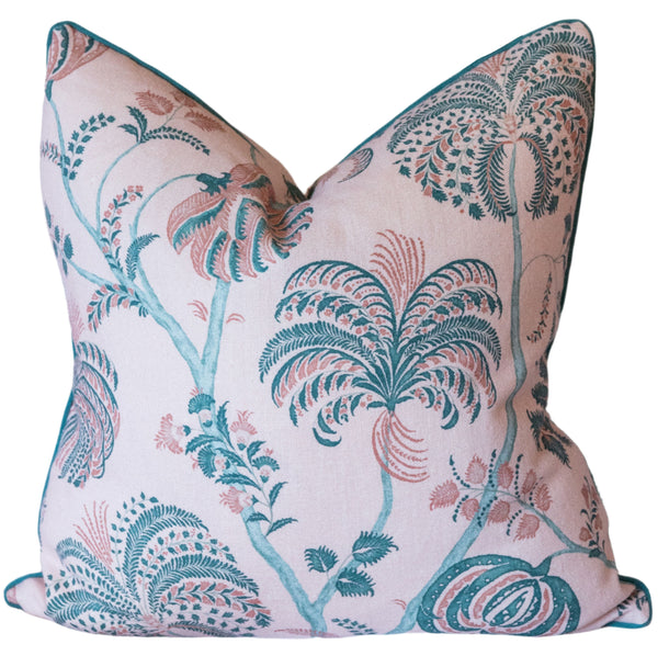 A Pink and Green Turquerie Pillow from Associated Design, featuring light pink down fill and a green tropical foliage pattern, is placed on a white sofa. Another 22" x 22" pillow with a geometric design is partially visible in the background.