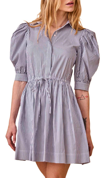 A person wearing the Hunter Bell NYC McCauley Dress, a short-sleeved, blue and white striped outfit with a gathered drawstring waist and puffed shoulders. The dress features a collar and front buttons, creating a universally flattering silhouette.