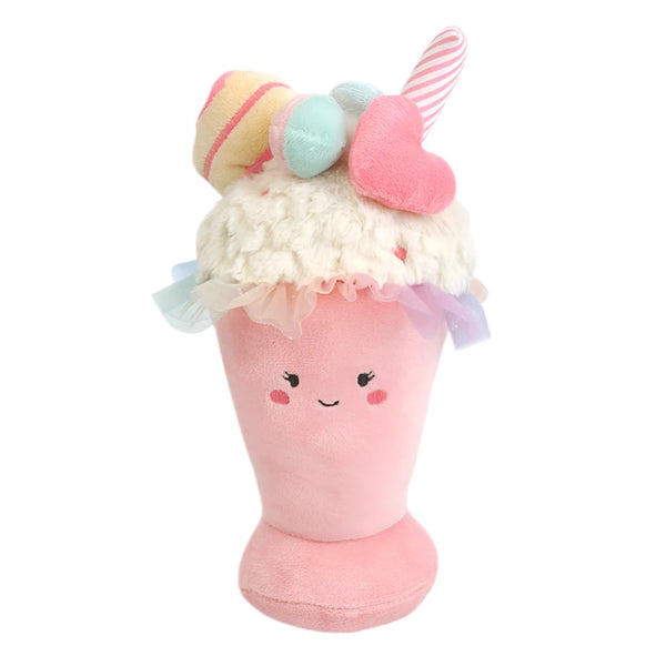 Introducing the MON AMI Sweet Treat Milkshake toy by Mon Ami: a plush delight resembling a pink milkshake with a smiling face, topped with fabric ice cream scoops, candy, and a heart. Complete the fun by pairing it with a colorful rainbow tutu for an extra touch of sweetness!