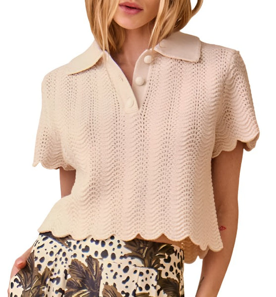 A person wearing the Hunter Bell NYC Nadine Sweater, a cream-colored, short-sleeve top made from Responsible Merino Wool with a scalloped hem and three buttons, paired with a patterned skirt featuring black, white, and yellow designs.