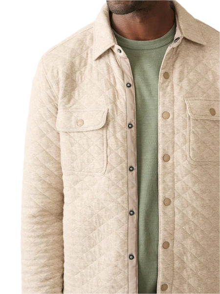 A person wearing the Faherty Epic Quilted Fleece, a beige jacket over a green t-shirt, showcasing a midweight masterpiece with its button-up front and two chest pockets.