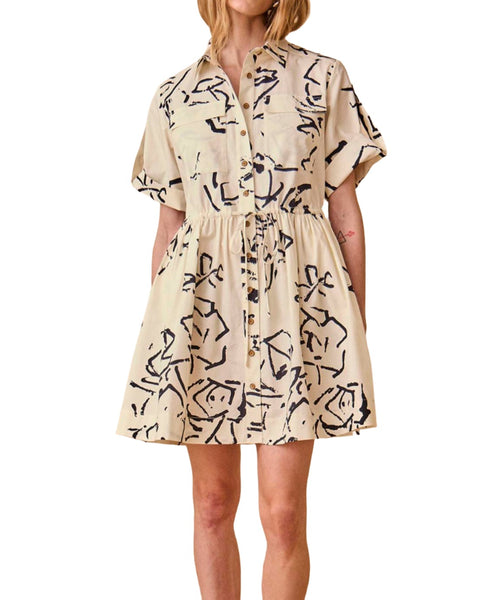 Person wearing a beige Hunter Bell NYC Peyton Dress with black abstract patterns and a collared neckline, standing against a white background. The dress features an adjustable drawcord waist for a tailored fit.