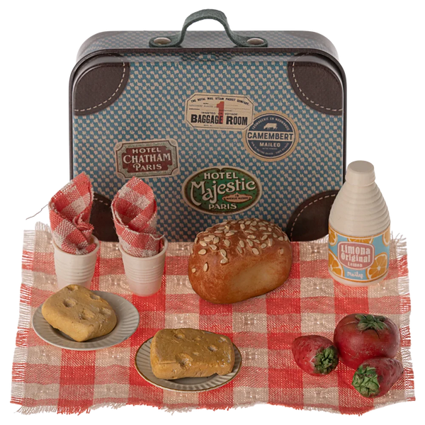 The Maileg Picnic Set by Maileg features a charming collection of a small vintage-style metal suitcase and assorted miniature food items, including bread, tomatoes, drinks, napkins, and plates, all arranged on a red and white checkered cloth.