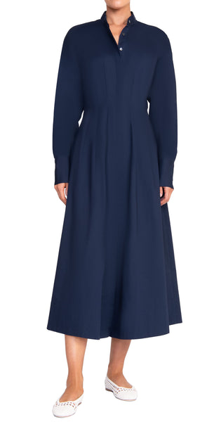 A person wearing the Staud Lorenza Midi Dress, a long-sleeved, button-up, full-length navy blue dress with an A-line skirt, and white shoes.