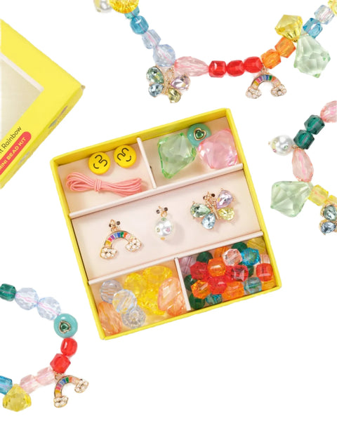 The Super Smalls Make It Rainbow Mini Bead Kit by Super Smalls is a vibrant assortment of colorful beads, rainbow and smiley face charms, elastic strings, and finished jewelry pieces, all housed in a cheerful yellow box. Perfect for inspiring unique creativity in crafters of all ages!